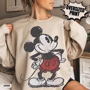 Puede incluir: Sudadera color arena con un gran gr&aacute;fico de Mickey Mouse en negro, rojo y blanco. El texto "OVERSIZED PRINT" est&aacute; en un bocadillo negro. La palabra "SAND" est&aacute; impresa en la parte inferior izquierda.