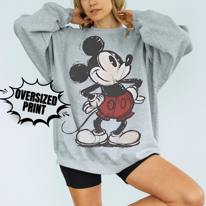 Puede incluir: Una sudadera gris de gran tama&ntilde;o con un gr&aacute;fico desgastado de Mickey Mouse en negro, rojo y blanco. El texto "OVERSIZED PRINT" est&aacute; en un bocadillo en blanco y negro. La sudadera tiene mangas largas.