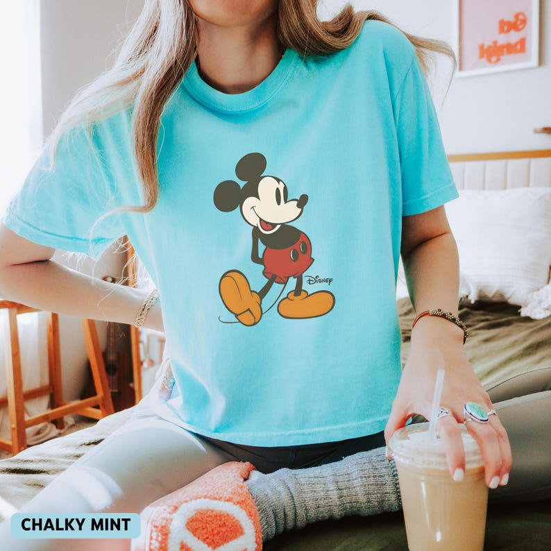 Puede incluir: Camiseta azul claro con un dise&ntilde;o de Mickey Mouse. El personaje de dibujos animados lleva pantalones cortos rojos y zapatos amarillos. La camiseta tiene la inscripci&oacute;n "Disney" y "Chalky Mint".