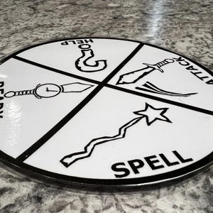 May include: A white, circular game piece with black borders and dividing lines. The piece is divided into four sections, each with a word and a corresponding icon: READY, HELP, ATTACK, and SPELL. The game piece has a glossy finish.