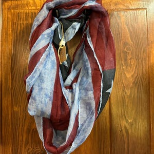 May include: A red, white, and blue patterned infinity scarf. The scarf is made of a soft, sheer fabric and features a faded, tie-dye effect.