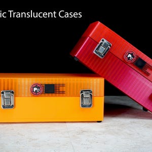 May include: Two rectangular U87 Mic Translucent Cases, one orange and one red, featuring silver metal latches, a textured surface, and a circular logo with the letters PD on the front. The cases are positioned against a black background.