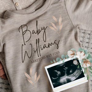 May include: A light brown onesie with the text "Baby Williams Arriving May 2025" and a black and white ultrasound image.
