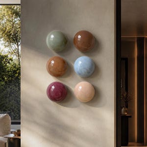 May include: A set of six circular, glossy wall-mounted decorative objects arranged in two columns. The spheres feature smooth, reflective surfaces in various solid and marbled colours, including sage green, brown, light blue, deep red, and peach.