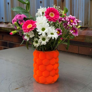 Peut inclure: Un bouquet de fleurs roses, blanches et violettes dans un vase orange vif au design texturé et ondulé.