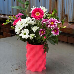 Peut inclure: Un vase cylindrique rose ondulé contenant un bouquet de fleurs blanches et roses. Les fleurs comprennent des marguerites blanches, des œillets roses et des gerberas roses.