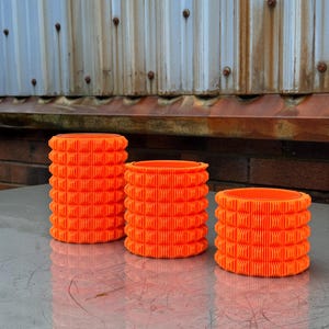 Peut inclure: Trois rouleaux en mousse orange de différentes tailles. Les rouleaux ont une surface texturée et sont conçus pour le massage et la récupération musculaire.