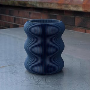 Peut inclure: Un vase cylindrique bleu foncé ondulé avec une texture côtelée.
