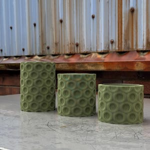 Peut inclure: Trois pots en céramique verts avec un design ondulé et texturé. Les pots sont disposés en rangée sur une surface argentée.