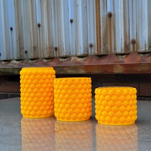 May include: Three yellow ceramic planters with a textured, bubble-like design. The planters are arranged in a row from largest to smallest.