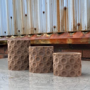 Peut inclure: Trois pots cylindriques en carton brun avec une texture ondulée. Les pots sont disposés en rangée du plus grand au plus petit sur une surface argentée.