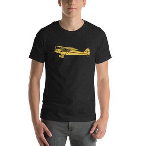 Op de afbeelding: Een donkergrijs t-shirt met een gele omtrek van een vintage vliegtuig. Het vliegtuigontwerp is gecentreerd op de borst. Het shirt is gemaakt van een zacht materiaal en heeft korte mouwen.