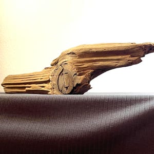 Könnte beinhalten: Ein Stück Treibholz mit natürlichem, verwittertem Aussehen. Das Holz ist hellbraun mit sichtbarer Maserung und Knoten, was darauf hindeutet, dass es von den Elementen geformt wurde. Das Treibholz liegt horizontal.