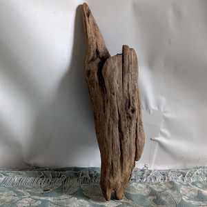 Könnte beinhalten: Ein Stück Treibholz mit rauer, strukturierter Oberfläche. Das Holz hat eine natürliche braune Farbe mit sichtbarer Maserung und Knoten. Das Treibholz hat eine unregelmäßige Form mit einer spitzen Spitze und einer breiteren Basis. Es wirkt verwittert und gealtert.
