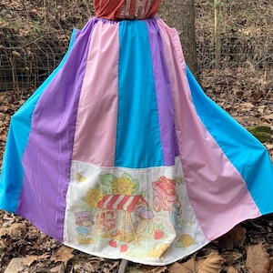 May include: A colorful maxi dress with a striped skirt in shades of purple, pink, blue, and white. The top is a red tank top with the text "Do Some Th" printed on it. The skirt has a Strawberry Shortcake print at the bottom.
