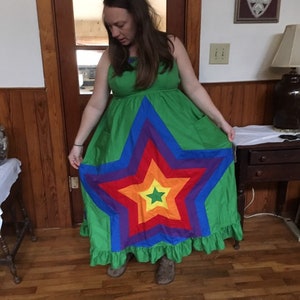 May include: A long green maxi dress with a rainbow star design. The dress has a ruffled hem and pockets on the sides.