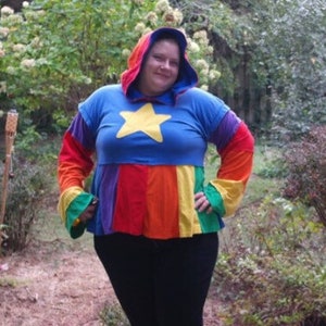 May include: A person wearing a blue hooded sweatshirt with a yellow star on the front. The sweatshirt has rainbow colored stripes on the bottom.