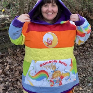 May include: A rainbow-colored hoodie with a quilted design and a large pocket featuring a Rainbow Brite character and the text "Rainbow Brite".