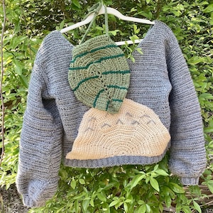 May include: A gray crocheted sweater with a large green and brown crocheted applique of a leaf and a smaller beige crocheted applique of a mountain.