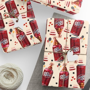May include: Gift wrap featuring a repeating pattern of Dr. Pepper cans and bottles wearing party hats, along with birthday cake illustrations, balloons, and stars. The wrapped gifts are tied with twine and have heart-shaped tags. A ball of twine and scissors are also visible.