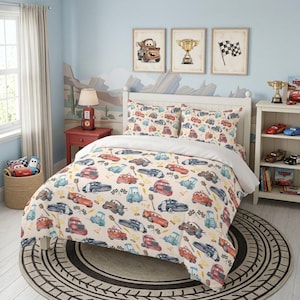May include: A twin bed featuring a cream-colored comforter and two matching pillow shams decorated with a repeating pattern of red, blue, and brown cartoon race cars, checkered flags, and gold trophies on a light-colored bedroom floor.