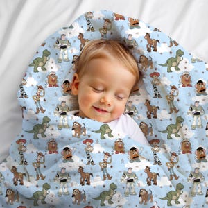 K&ouml;nnte beinhalten: Eine hellblaue Fleecedecke mit einem sich wiederholenden Muster aus Toy Story-Figuren wie Woody, Buzz Lightyear, Rex, Slinky Dog, Jessie und Mr. Potato Head, durchsetzt mit wei&szlig;en Wolken und kleinen Sternen auf dem gesamten Stoff.