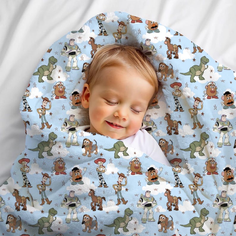 K&ouml;nnte beinhalten: Eine hellblaue Fleecedecke mit einem sich wiederholenden Muster aus Toy Story-Figuren wie Woody, Buzz Lightyear, Rex, Slinky Dog, Jessie und Mr. Potato Head, durchsetzt mit wei&szlig;en Wolken und kleinen Sternen auf dem gesamten Stoff.