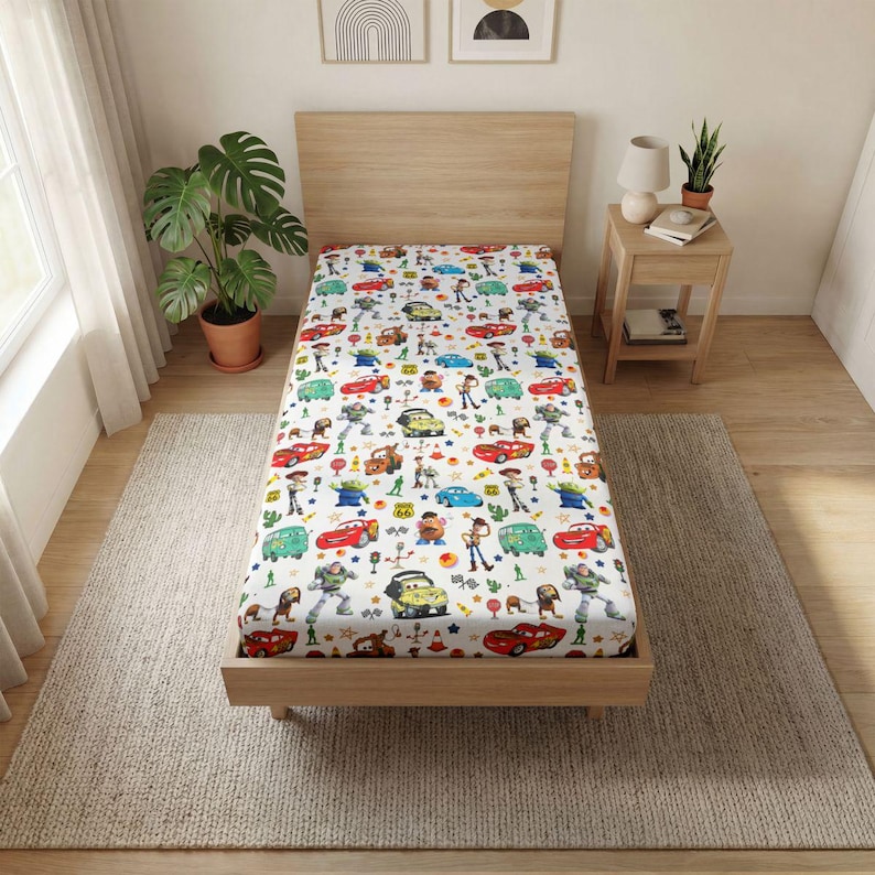 May include: A twin-sized bed featuring a white fitted sheet with a repeating pattern of various animated characters, including red race cars, space rangers, cowboys, potato-shaped figures, and green aliens, interspersed with small traffic cones and stars.
