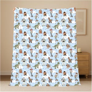 K&ouml;nnte beinhalten: Eine hellblaue Fleecedecke mit einem sich wiederholenden Muster aus Toy Story-Figuren wie Woody, Buzz Lightyear, Jessie, Rex, Mr. Kartoffelkopf, Slinky Dog und Bullseye, durchsetzt mit kleinen wei&szlig;en Wolken und braunen Sternformen.