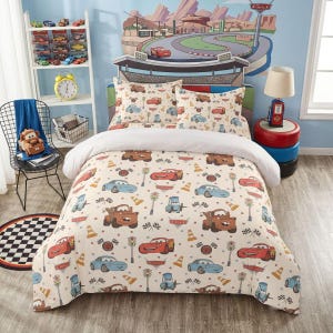 May include: A twin-sized bed set featuring a cream-colored comforter and two matching pillowcases decorated with a repeating pattern of cartoon race cars, traffic cones, and checkered flags. The headboard displays a large graphic of a racetrack.