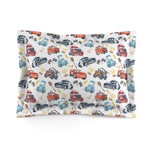 K&ouml;nnte beinhalten: Wei&szlig;es Kopfkissen mit einem sich wiederholenden Muster von Cartoon-Autos in verschiedenen Farben. Das Design umfasst Rennwagen, Polizeiautos und Lastwagen sowie karierte Flaggen, Troph&auml;en und andere Elemente zum Thema Rennen. Ein lustiges und farbenfrohes Bettzubeh&ouml;r.