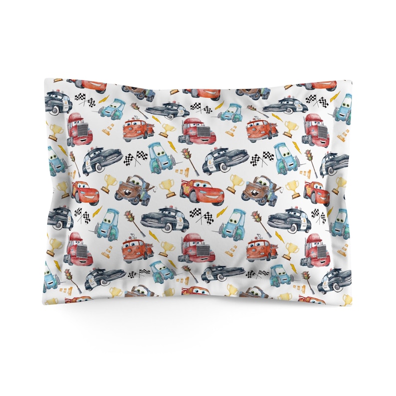 K&ouml;nnte beinhalten: Wei&szlig;es Kopfkissen mit einem sich wiederholenden Muster von Cartoon-Autos in verschiedenen Farben. Das Design umfasst Rennwagen, Polizeiautos und Lastwagen sowie karierte Flaggen, Troph&auml;en und andere Elemente zum Thema Rennen. Ein lustiges und farbenfrohes Bettzubeh&ouml;r.
