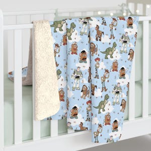K&ouml;nnte beinhalten: Eine hellblaue Fleecedecke mit einem sich wiederholenden Muster aus Toy Story-Figuren wie Woody, Buzz Lightyear, Rex, Mr. Potato Head, Jessie, Bullseye und Slinky Dog, durchsetzt mit wei&szlig;en Wolken und kleinen Sternen auf einem weichen Stoff.
