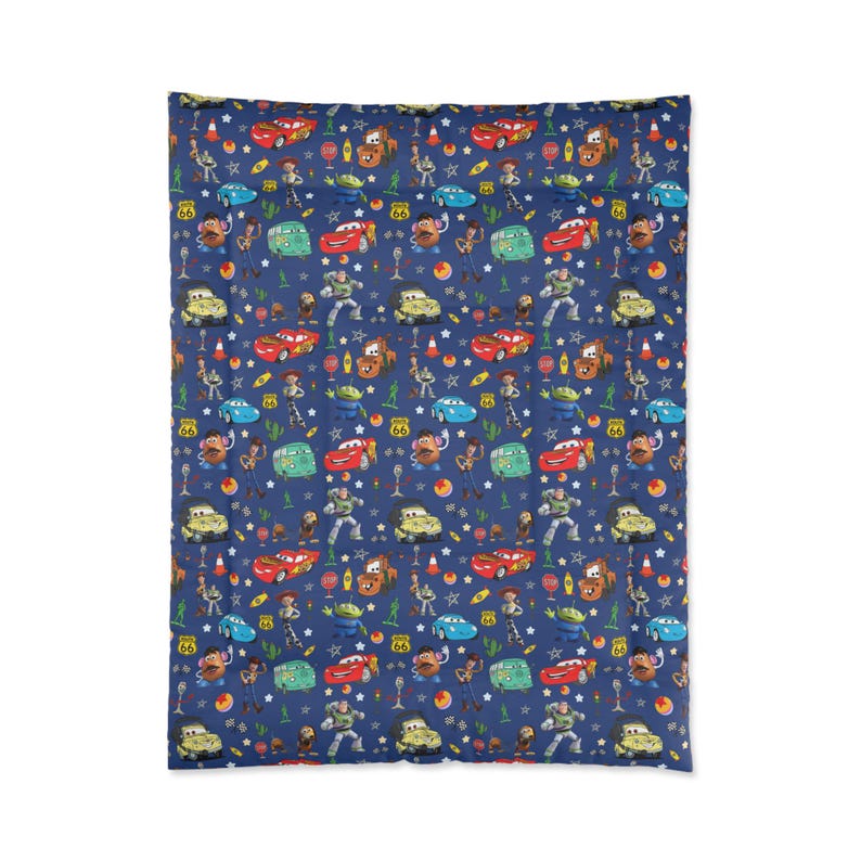 May include: A rectangular blanket featuring a dark blue background with a repeating pattern of characters from the Cars and Toy Story movies, including red race cars, green aliens, cowboys, and potato figures, interspersed with stars and road signs.