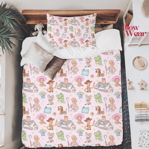 May include: Pink bedding set featuring a repeating pattern of cartoon characters, including a cowboy, space ranger, dinosaur, and other toys. The set includes a pillowcase and a comforter, perfect for a child's bedroom.