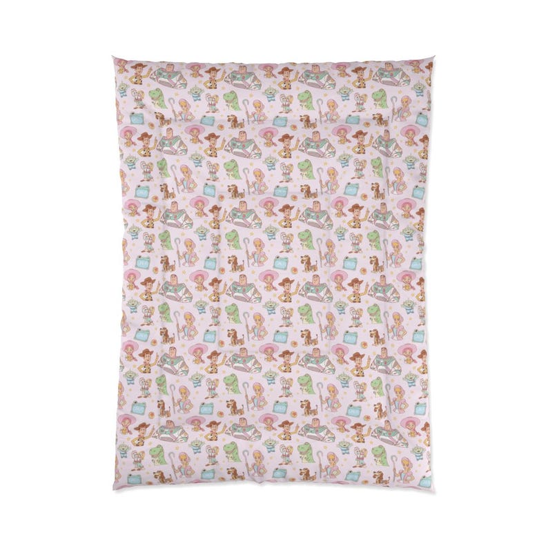 May include: A rectangular blanket featuring a repeating pattern of Toy Story characters including Woody, Buzz Lightyear, Bo Peep, Rex, and Slinky Dog on a light pink background. The design includes small stars and blue shapes scattered throughout.