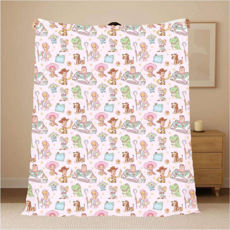 May include: A pink blanket with a repeating pattern of cartoon characters, including a cowboy, space ranger, and dinosaur. The blanket has a soft, plush appearance and is likely made of a comfortable material. The design includes stars and other elements.