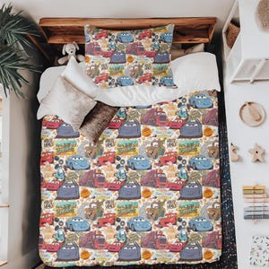 Pode incluir: Conjunto de roupa de cama branco com um padr&atilde;o repetido de carros de desenho animado, sinais da Rota 66 e gr&aacute;ficos relacionados. O design apresenta carros em azul, vermelho e cinza, criando uma est&eacute;tica vibrante e l&uacute;dica.