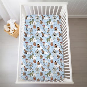 May include: A light blue crib sheet featuring a repeating pattern of Toy Story characters including Woody, Buzz Lightyear, Jessie, Rex, Slinky Dog, and Mr. Potato Head, interspersed with small white clouds and stars across the fabric surface.