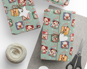 Puede incluir: Papel de regalo con un patrón repetitivo de personajes de Disney, incluidos Mickey Mouse, Minnie Mouse, el Pato Donald y Pluto con gorros de Papá Noel, intercalados con bastones de caramelo y copos de nieve sobre un fondo verde claro, atado con cordel.