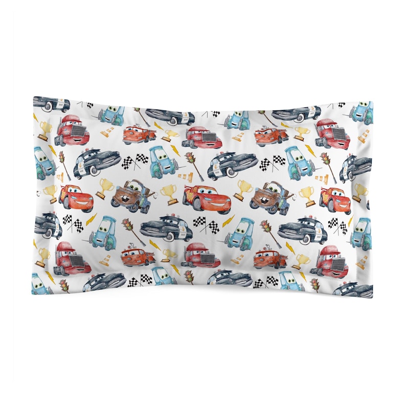 K&ouml;nnte beinhalten: Rechteckiger, wei&szlig;er Kissenbezug mit einem sich wiederholenden Muster von Cartoon-Autos in verschiedenen Farben. Das Design umfasst Rennwagen, Polizeiautos und Abschleppwagen sowie Zielflaggen und Troph&auml;en.