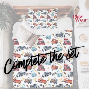 K&ouml;nnte beinhalten: Ein wei&szlig;es Bettw&auml;sche-Set mit einem bunten Automuster. Das Design umfasst verschiedene Cartoon-Autos, Schachflaggen und Troph&auml;en. Der Text "Complete the set" steht unten. Kissenbezug und Bettbezug sind sichtbar.