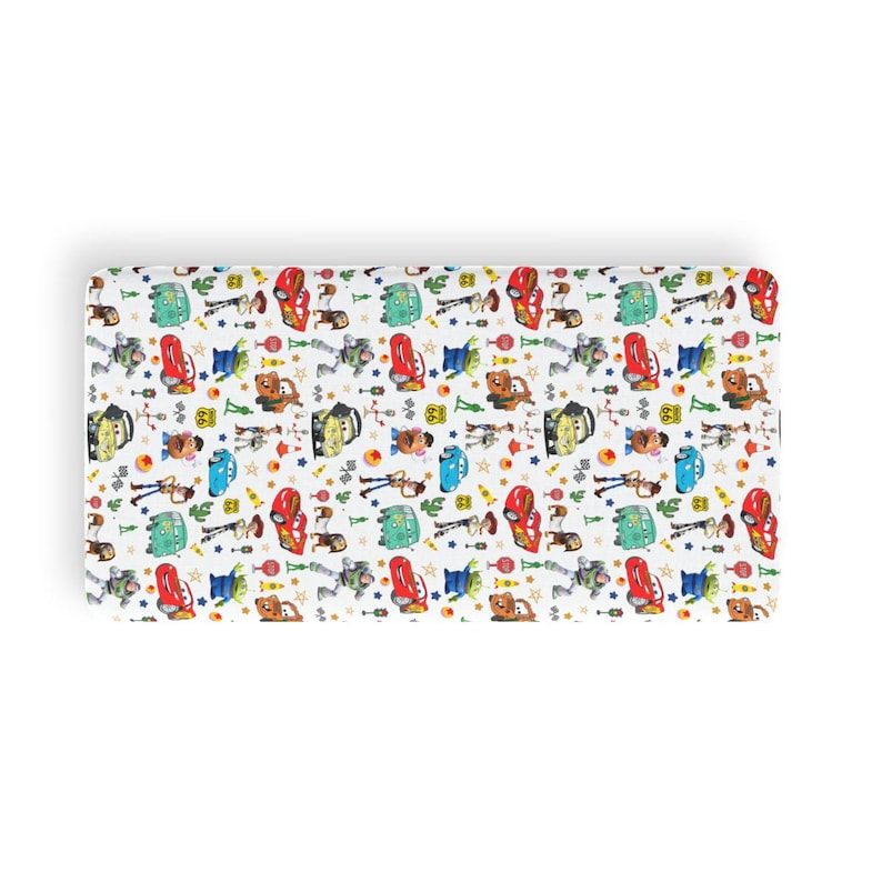 May include: A rectangular fabric sheet featuring a repeating pattern of various animated characters and vehicles on a white background. The print includes red race cars, blue cars, green vans, and figures of cowboys, space rangers, and potato-shaped toys.