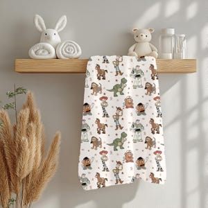May include: A white hand towel featuring a repeating pattern of Toy Story characters, including Woody, Buzz Lightyear, and Rex. The towel is hanging on a wooden shelf with decorative items.