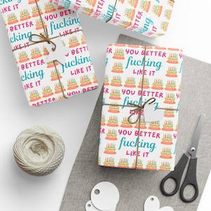 May include: Birthday-themed gift wrap featuring a cake pattern and the phrase "YOU BETTER fucking LIKE IT". The gifts are tied with twine and have blank tags. A ball of twine and scissors are also visible, alongside some blank tags.