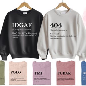 May include: Twelve different designs for sweatshirts with humorous acronyms and definitions. The designs include IDGAF, 404, SMH, YOLO, TMI, FUBAR, and DILLIGAF.