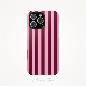 May include: A phone case with a vertical striped pattern in shades of pink and burgundy. The case has a camera module with three lenses and a flash. The brand name "Moonie's Cases" is printed at the bottom.