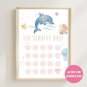 May include: A framed print with a watercolour illustration of a dolphin, starfish, and coral reef. The print includes the German phrase "Ich schaffe das!" and pink circles for tracking progress. A pink circle in the bottom right corner has the text "A4 PDF ZUM AUSDRUCKEN".