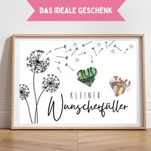May include: A framed print featuring a dandelion design with money shaped as hearts. The text "DAS IDEALE GESCHENK" is at the top, and "KLEINER WUNSCHERFÜLLER" is written below the hearts. The frame is light brown.