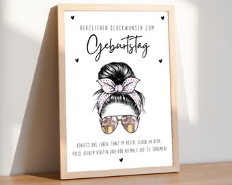 May include: A framed print with the text "HERZLICHEN GLÜCKWUNSCH ZUM Geburtstag" and a drawing of a woman with sunglasses and a bow in her hair. The print also includes the text "GENIESS DAS LEBEN, TANZ IM REGEN, GLAUB AN DICH. FOLGE DEINEM HERZEN UND HÖR NIEMALS AUF ZU TRÄUMEN!"